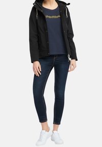 Mustat hupparitakki, jossa on vetoketjut, laivastonsininen T-paita, jossa on kultaiset kirjainpainatukset, slim-fit tummat farkut ja valkoiset lenkkarit. Rentoa pukeutumista, minimalistisia yksityiskohtia.