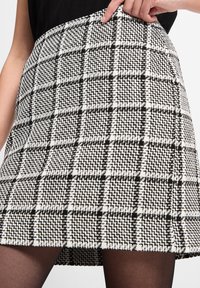 Schwarz-weißer karierter Rock aus strukturiertem Stoff, mit ausgestellter Silhouette und sichtbarem Saum. Betont durch ein kariertes Muster.