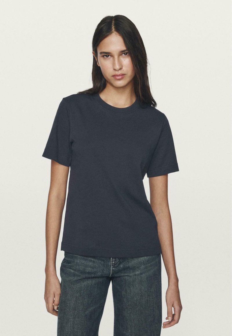 T-shirt in cotone blu navy con maniche corte, scollo rotondo, forma aderente e texture morbida, abbinato a jeans in denim scuri.