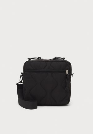 Sac de bandoulière noir matelassé avec un motif en vagues texturé, poche avant zippée, sangle réglable et en matériau nylon.