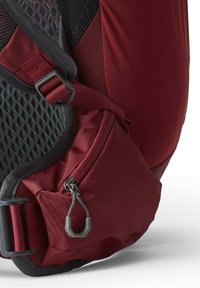 Maroon backpack detail featuring mesh fabric, adjustable straps, and a zippered pocket with a gray pull. Textured panels add visual interest.