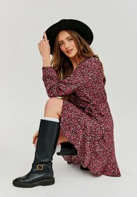 Kvetinová šaty po kolená v ružovej a bielej farbe s dlhými rukávmi. Nosí sa s čiernymi koženými čižmami po kolená s popruhom a prackou.