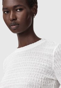 Witte gebreide top met structuur en een golvend patroon, met een ronde halslijn en subtiele ribgebreide accenten. Korte mouwen en lichtgewicht stof.