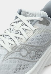 Chaussure de course Saucony blanche et grise avec une empeigne en mesh, logo détaillé sur le côté, et lacets blancs noués en croix.