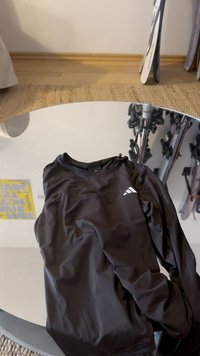 Zwart atletisch shirt met lange mouwen en een gladde textuur. Voorzien van een klein wit logo op de borst en een ronde hals.