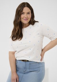 Jasnokremowy T-shirt z krótkim rękawem w niebieskie wzory serc, z okrągłym dekoltem, w połączeniu z wysokim stanem niebieskich dżinsów i czarnym paskiem.