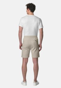 Pantaloni corti beige realizzati in tessuto morbido, dotati di una tasca posteriore, abbinati a una maglietta bianca semplice. L'outfit è completato da sneakers bianche.