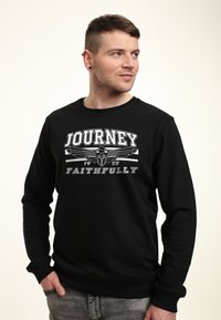 Schwarzer Pullover mit Rundhalsausschnitt, der einen weißen Grafikdruck mit den Worten "JOURNEY" und "FAITHFULLY" auf einem einfarbigen Hintergrund zeigt.