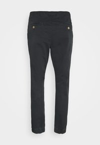 Pantalons en coton extensible noirs avec taille élastique, deux poches arrière et chevilles resserrées. Texture lisse et sans motifs visibles.