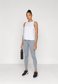 Λευκό αθλητικό φανελάκι, γκρι κολάν, μαύρα αθλητικά παπούτσια και μια μαύρη παγούρι νερού. Περιλαμβάνει ένα λογότυπο στο πουκάμισο και εφαρμοστή σχεδίαση.