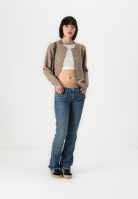 Cardigan de lã bege com botões à frente, combinado com uma t-shirt cropped branca e jeans de ganga azuis. Ténis pretos com riscas brancas incluídos.