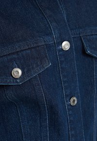 Mörkblå denimjacka med silverfärgade tryckknappar och en vikt krage, med synliga sömmar och en klassisk design.