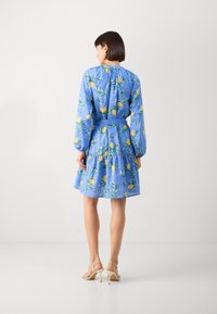 Rochie florală albastră cu model de lămâie și frunze, cu mâneci lungi, tiv în straturi și talie ajustată. Purtați cu sandale cu toc bej.