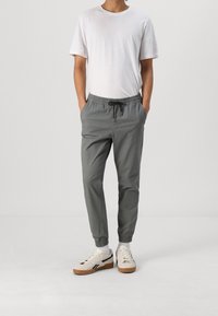 Ljust grå joggerbyxor med elastisk midja och dragsko, tillsammans med en enkel vit t-shirt med kort ärm och beige sneakers.