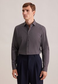 Marineblauw overhemd met een geometrisch patroon in rood, wit en lichtblauw. Heeft een kraag en lange mouwen; gecombineerd met donkere broeken.
