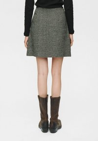 Fustă gri cu model houndstooth, confecționată dintr-un material texturat, cu un design evazat și o margine deasupra genunchiului, asortată cu cizme din piele maro, până la genunchi.