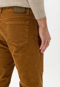 Bruna kordflöjelbyxor med rak skärning. Försedda med bakfickor och ett märkesläderlappar vid midjan. Texturen är ribbad.