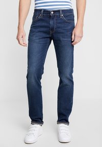 Mörkblå denimjeans med rak passform, utrustade med fem fickor, bältesöglor och kontrasterande sömmar. Bärs med vita sneakers.