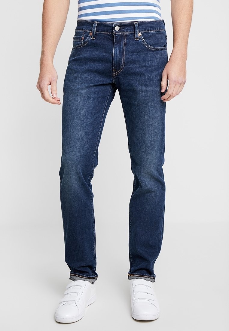Mörkblå denimjeans med rak passform, utrustade med fem fickor, bältesöglor och kontrasterande sömmar. Bärs med vita sneakers.