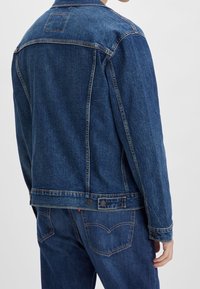 Chaqueta de mezclilla en azul oscuro, con cuello clásico, puños abotonados, dos pliegues en la espalda, etiqueta de Levi's en la parte posterior y detalles de costura en contraste.