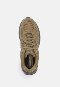Chaussure de sport beige avec une tige en mesh, un col rembourré et une semelle en caoutchouc texturée. Dotée de lacets et d'un branding discret sur le côté.