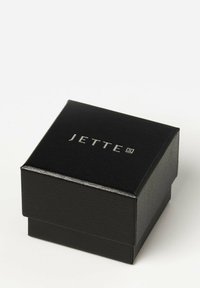 Sort smykkeboks lavet af tekstureret materiale, med et sølvfarvet "JETTE"-logo på låget. Kompakt og slankt design.