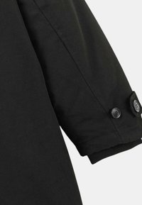 Manche de vêtement d'extérieur noir avec une texture lisse, dotée de deux boutons noirs au poignet pour l'ajustement. Design simple et structuré.