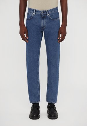 Blue denim straight-leg jeans with a faded finish, five pockets, and button closure, paired with black shoes.