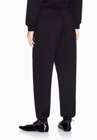 Zwarte sweatpants met een elastische tailleband en een boord aan de enkels, voorzien van zijzakken en een subtiele logo-detail. Gekocht met glanzend zwart schoeisel.