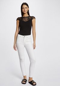 Haut noir avec des manches en dentelle, associé à un jean blanc et des sandales noires à glissière avec une boucle décorative.