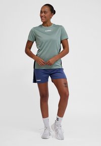 Light green athletic t-shirt with a crew neck and black side panels. Paired with navy shorts, featuring logo detailing and side stripes.