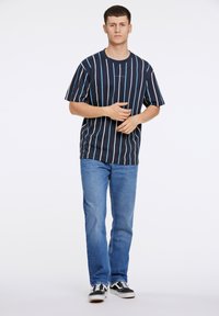 Marine gestreepte T-shirt met lichtblauwe verticale lijnen, gecombineerd met lichtblauwe denim jeans en zwarte sneakers. Eenvoudig, casual ontwerp.