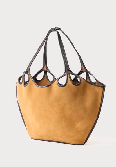 Tan suede tote bag with soft texture, featuring a unique open-top design and black leather accents. Four handles with cutout details.