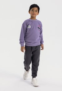 Felpa viola con vari patch, abbinata a pantaloni grigi e sneakers bianche. Tessuto morbido, vestibilità casual, polsini e vita a costine.