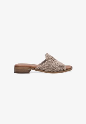 Beige woven slide sandal with a textured upper, closed toe, and low stacked heel. Features circular decorative accents and a smooth leather insole.