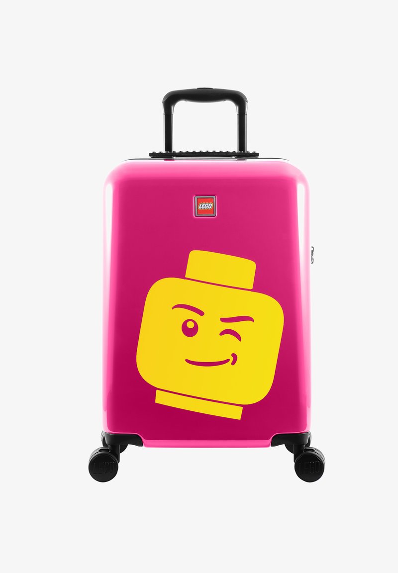 Tvrzený růžový kufr s černými kolečky. Na přední straně se nachází velká žlutá grafika hlavy LEGO a malé logo LEGO.