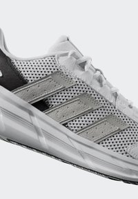 White athletic shoe with mesh upper, gray accents, and three signature stripes. Features a textured sole and detailed lacing system.