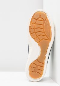 Sneaker sole with textured orange rubber and white edges. Features deep grooves for traction and "G-Star Raw" branding.