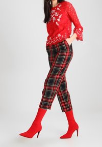 Top in pizzo rosso con motivi floreali abbinato a pantaloni tapered a quadri neri e rossi. Accessoriato con stivali alti con punta affusolata rossi.