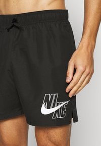 Zwarte zwembroek van lichtgewicht materiaal, met een elastische tailleband, een koord en een opvallend wit Nike-logo aan de linkerkant.