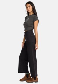 Dark gray cropped t-shirt with a graphic design, paired with high-waisted black wide-leg jeans and brown ankle boots with elastic sides.