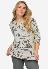 T-shirt à manches longues de couleur gris clair avec un imprimé d'oiseaux en gris foncé. Panneaux latéraux découpés avec des accents jaunes. Texture douce et coupe décontractée.