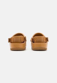 Brune vanntette sandaler med en glatt overflate, justerbare stropper og en teksturert såle. Diskret merkevare på hælen.