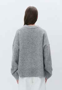 Pulôver cinza, oversized, feito de um tecido macio, apresentando uma bainha canelada e ombros caídos, com um decote arredondado e textura mínima.