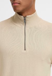Bežna zip-up jakna s visokim ovratnikom, izrađena od teksturiranog pletenog materijala, s metalnim srebrnim zatvaračem na vratu.