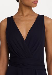 Navy blue dress with a V-neck, featuring pleated fabric and a wide waistband. Smooth texture and elegant draping detail at the bust.