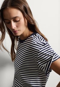 Camiseta de rayas en azul marino y blanco con mangas cortas y cuello redondo. El material parece suave y tiene una textura lisa.