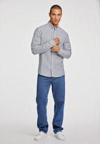 Camisa de cuadros en gris y blanco, con mangas largas, combinada con jeans de mezclilla azul y zapatillas blancas. Diseño sencillo, ajuste casual.