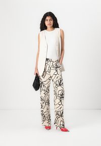 Light beige sleeveless vest over a white tank, paired with loose black floral print trousers and red pointed-toe heels. Black handbag included.