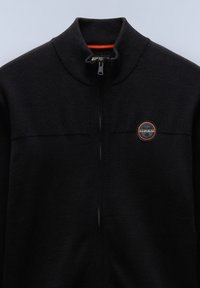 Sweat-shirt noir zippé avec un col montant, motif en tricot texturé. Présente un logo circulaire avec des accents orange sur le côté gauche.